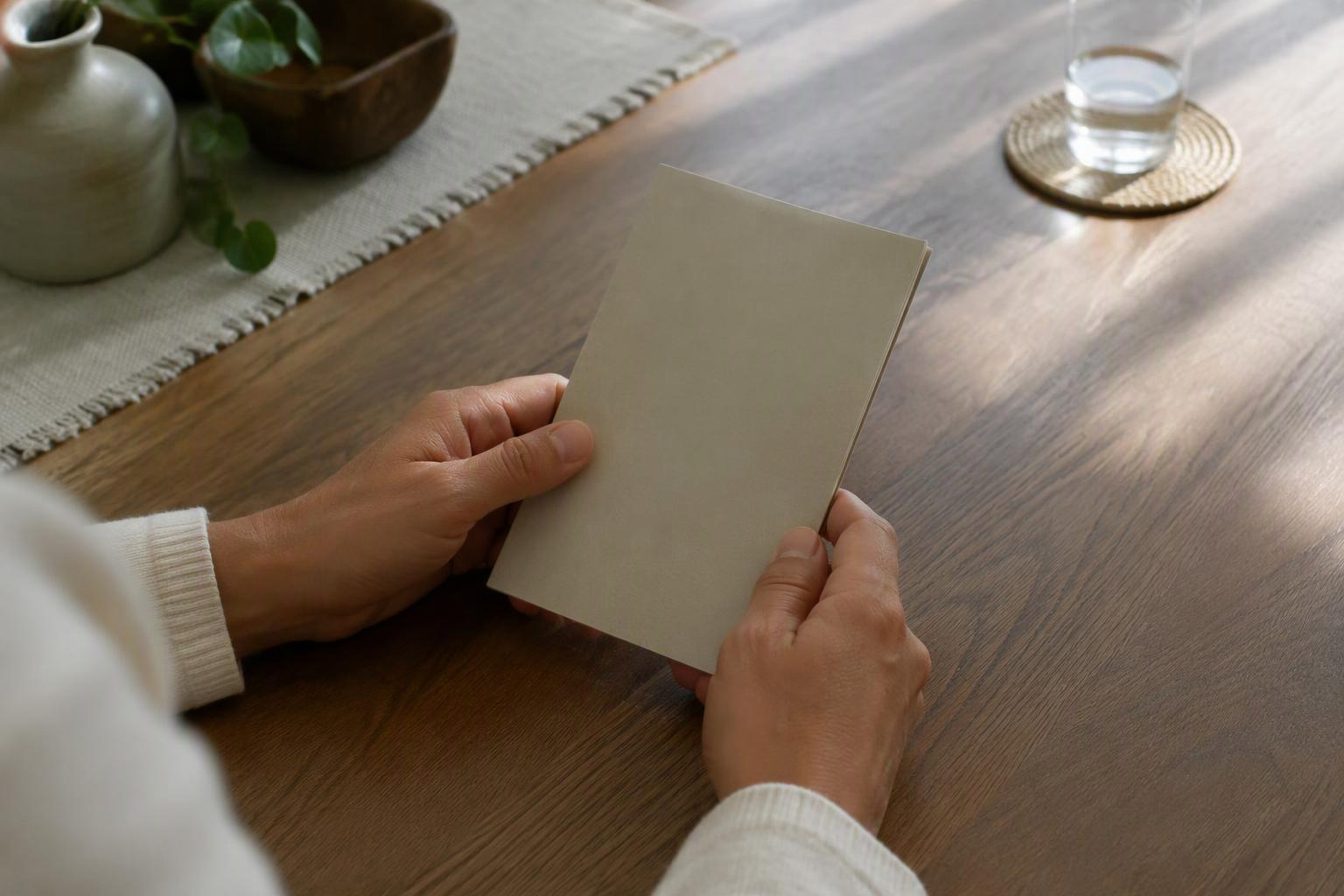 Mãos de uma pessoa adulta segurando uma carteira de papel fechada sobre uma mesa.